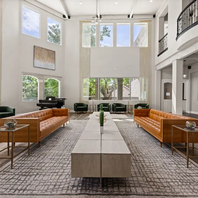 Elegant Modern Living Room A spacious modern living room featuring two leather sofas, a long coffee table, and large windows allowing natural light in. There are green accent chairs and artworks on the wall, complemented by a soft area rug.