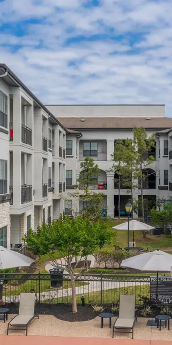 Exterior of Palazzo at Cypruswood apartments and pool lounge area and chairs with tables and umbrellas