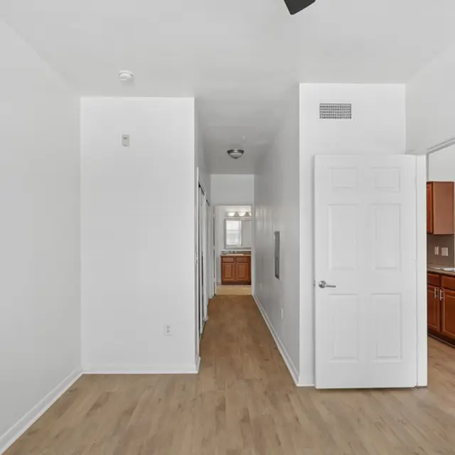 A modern hallway featuring light-colored walls, a wood floor, and several doorways leading to rooms