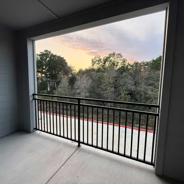 A balcony view showing trees and a colorful sunset in the background.
