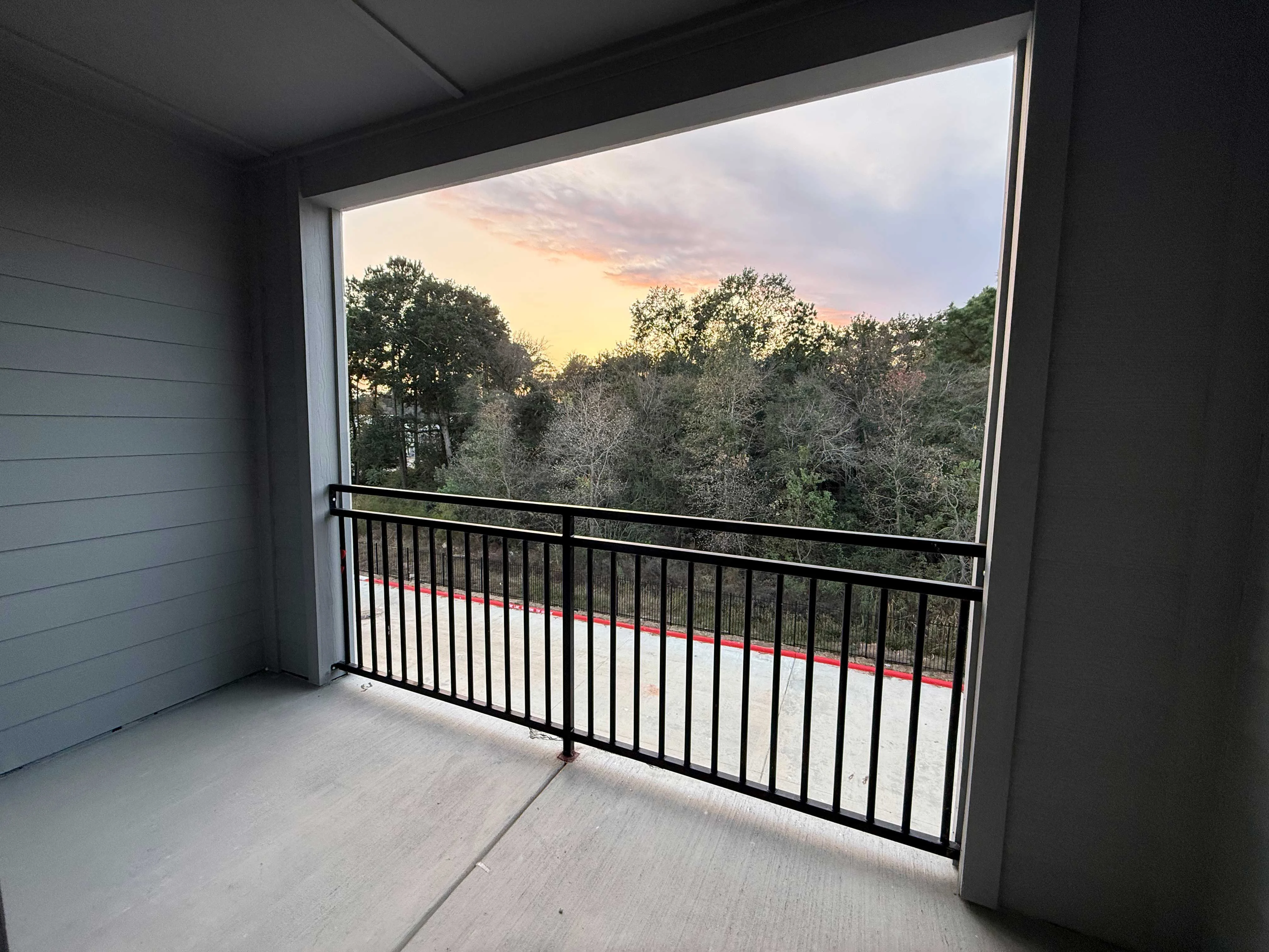 Balcony Sunset View A balcony view showing trees and a colorful sunset in the background.