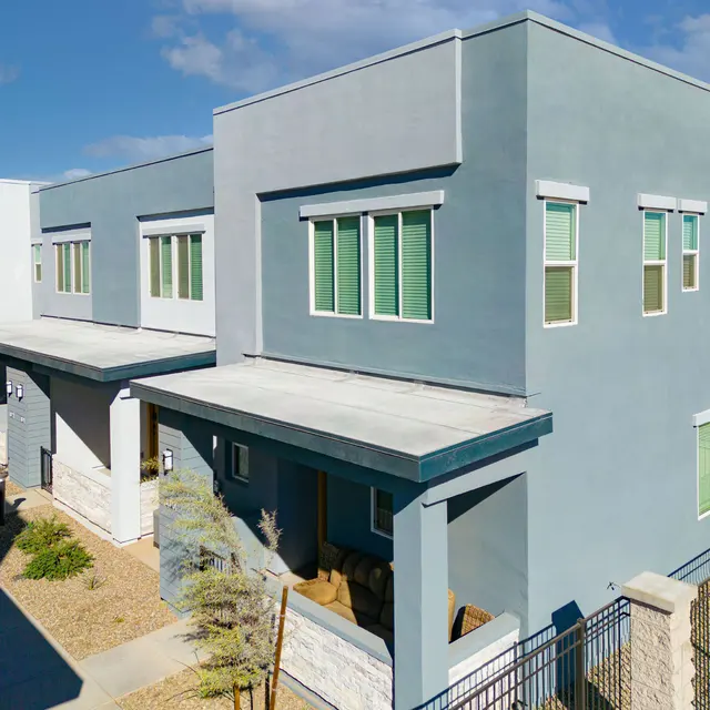 Modern Housing Complex A modern housing complex featuring two-story buildings with a flat roof, large windows, and a clean, minimalist design. The exterior is a mix of gray and light colors, with small gardens and a pathway in front.