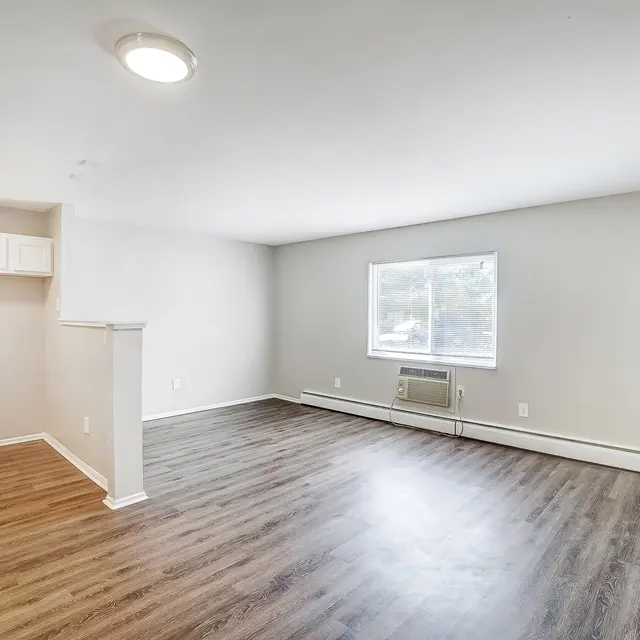 A spacious interior of a modern apartment featuring light-colored walls, a large window, and a clean open layout with wooden flooring.