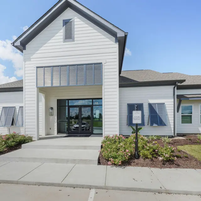 A modern white office building with large windows and a welcoming entrance, surrounded by landscaped areas and clear blue skies. Lafayette Youngsville