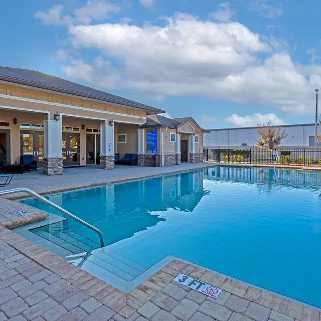 A serene swimming pool area with lounge chairs and a clubhouse in the background, surrounded by a well-maintained outdoor space.