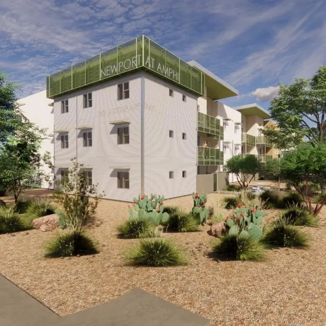 A modern multi-story apartment building surrounded by greenery and desert landscaping, including plants and rocks. A pathway leads through the landscaped area. The building features contemporary architecture with large windows and a green balcony area.