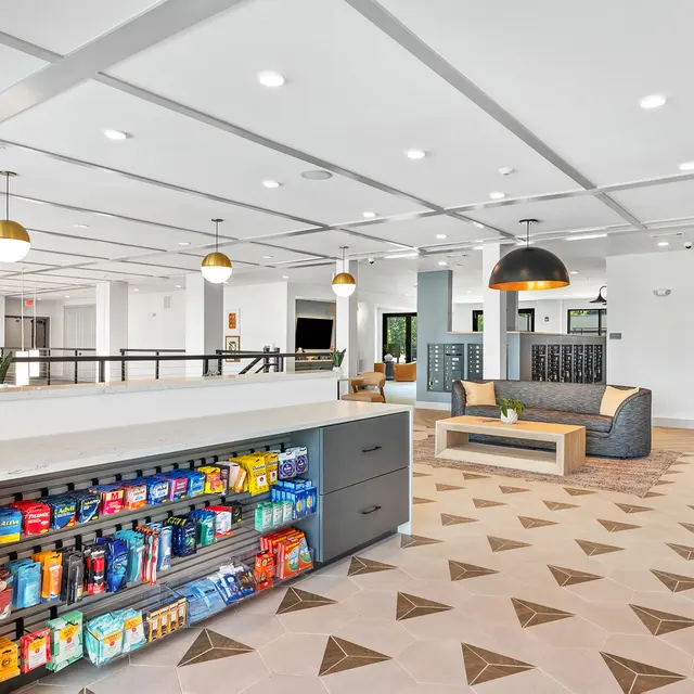 A spacious and modern lobby area featuring a service counter with a variety of snacks and drinks, a lounge area with seating, and decorative lighting fixtures.