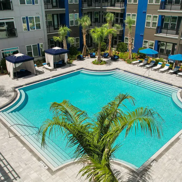 Modern Apartment Complex Pool Area Aerial view of a modern apartment complex pool area featuring a large swimming pool surrounded by palm trees and lounge chairs.