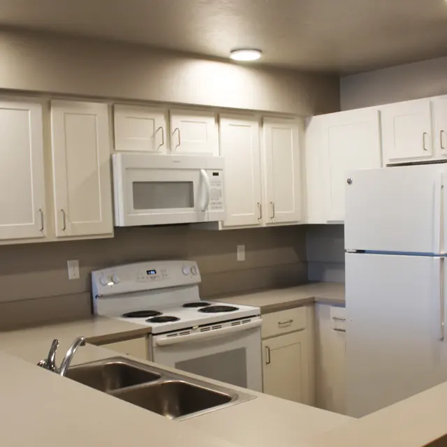 A modern kitchen featuring white cabinets, a white refrigerator, a stove, a microwave, and a sink area with a countertop.