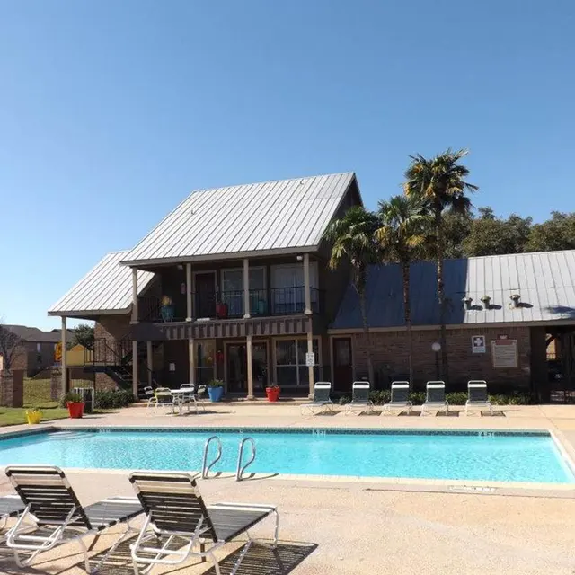 A scenic view of a pool area with lounge chairs and a building in the background.