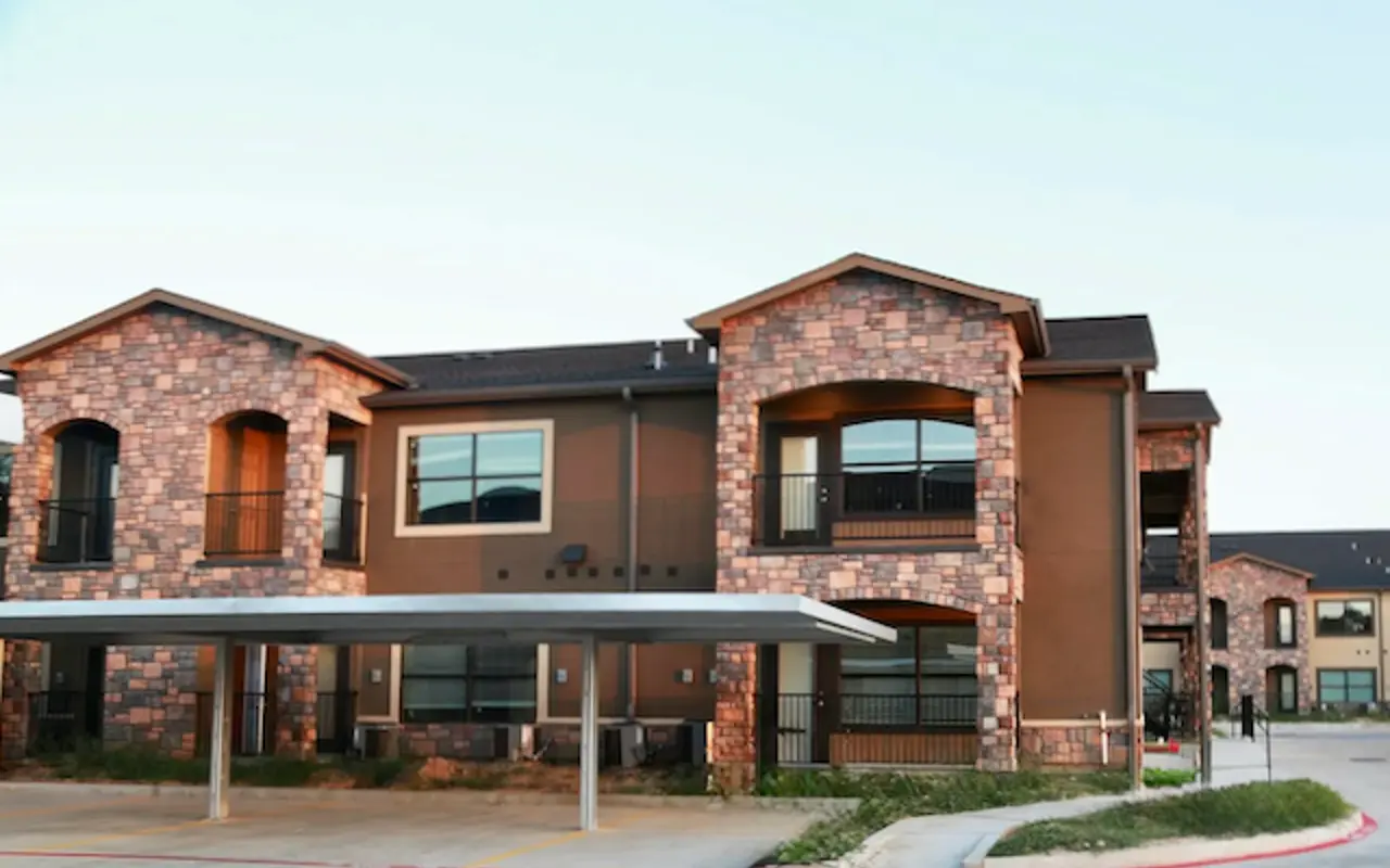 Exterior view of a modern apartment building featuring stone and stucco architecture with a covered parking area.