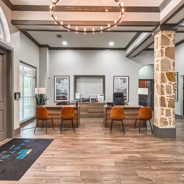 A modern office reception area featuring a stone column, wooden flooring, and contemporary seating. The reception desk is in the background with decorative artwork on the walls.