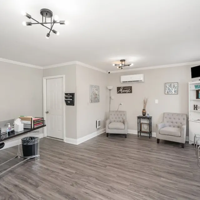 A modern office space featuring a desk with office supplies, two comfortable chairs, and light-colored walls with artwork.