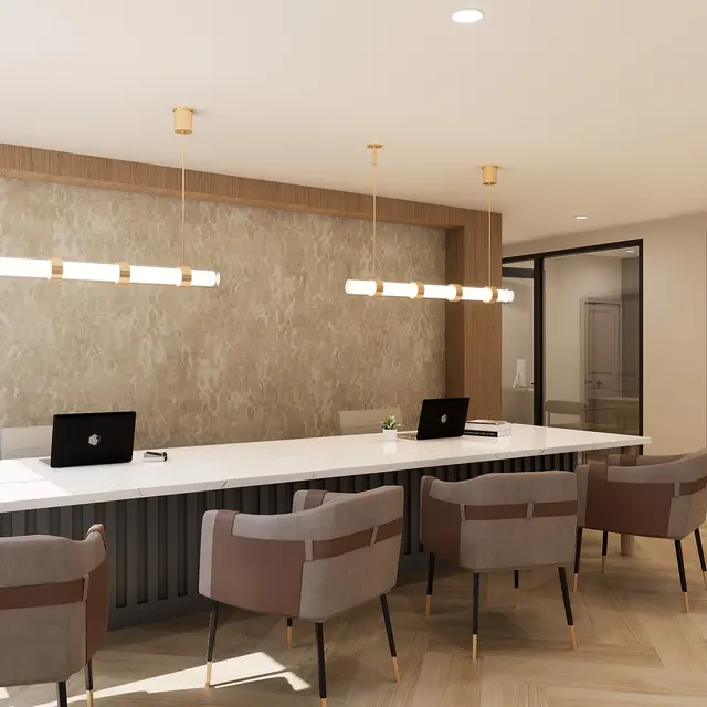 A modern office reception area featuring a long white desk with laptops, surrounded by plush chairs and warm lighting fixtures.