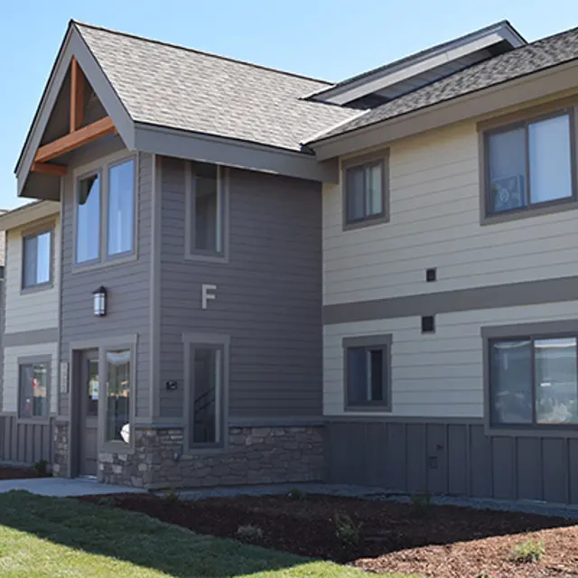 Modern Apartment Complex Exterior view of a modern apartment complex featuring a combination of gray and beige siding with stone accents, and a landscaped pathway.