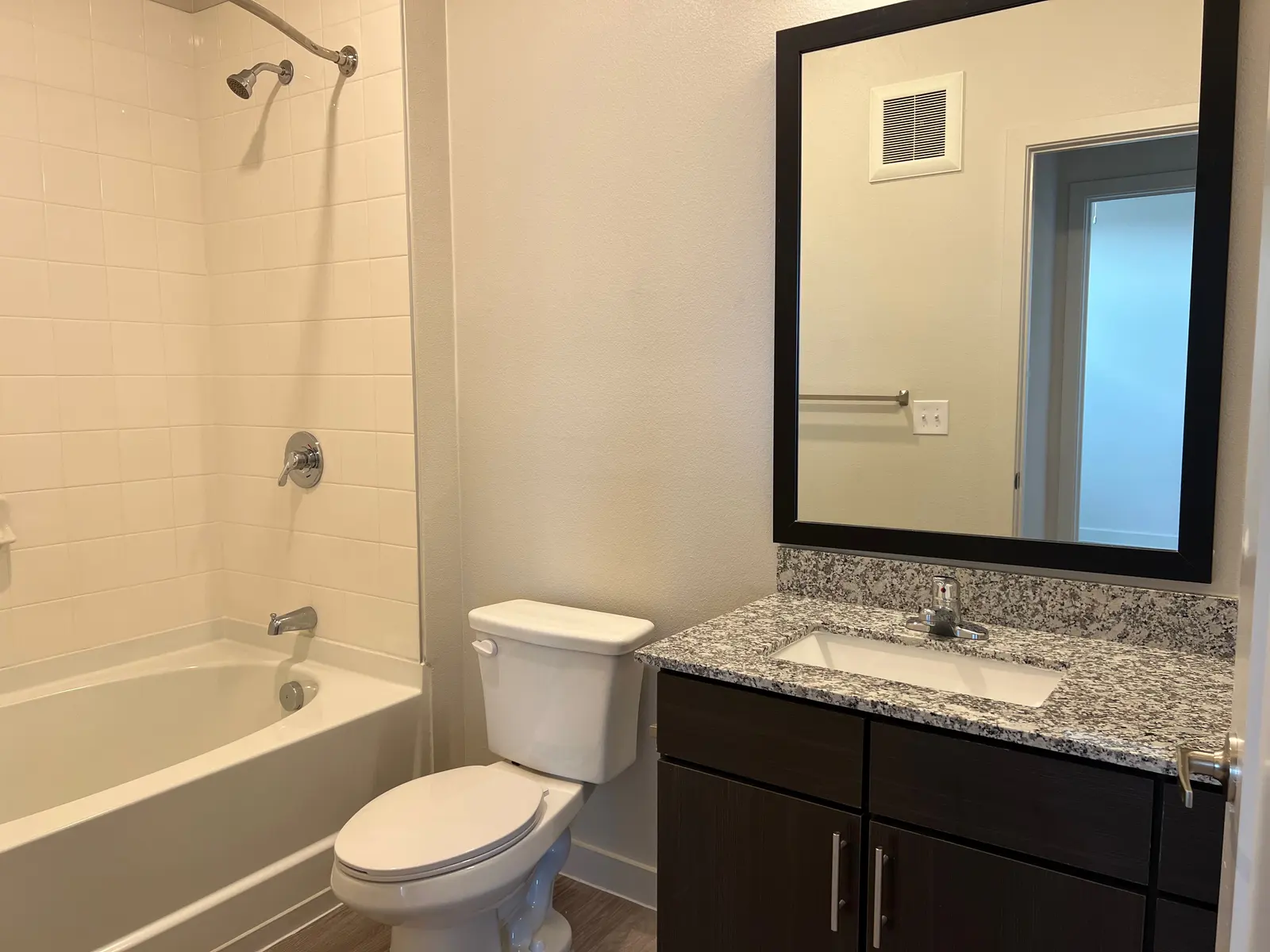 A modern bathroom featuring a bathtub, toilet, and a vanity with a granite countertop and large mirror.