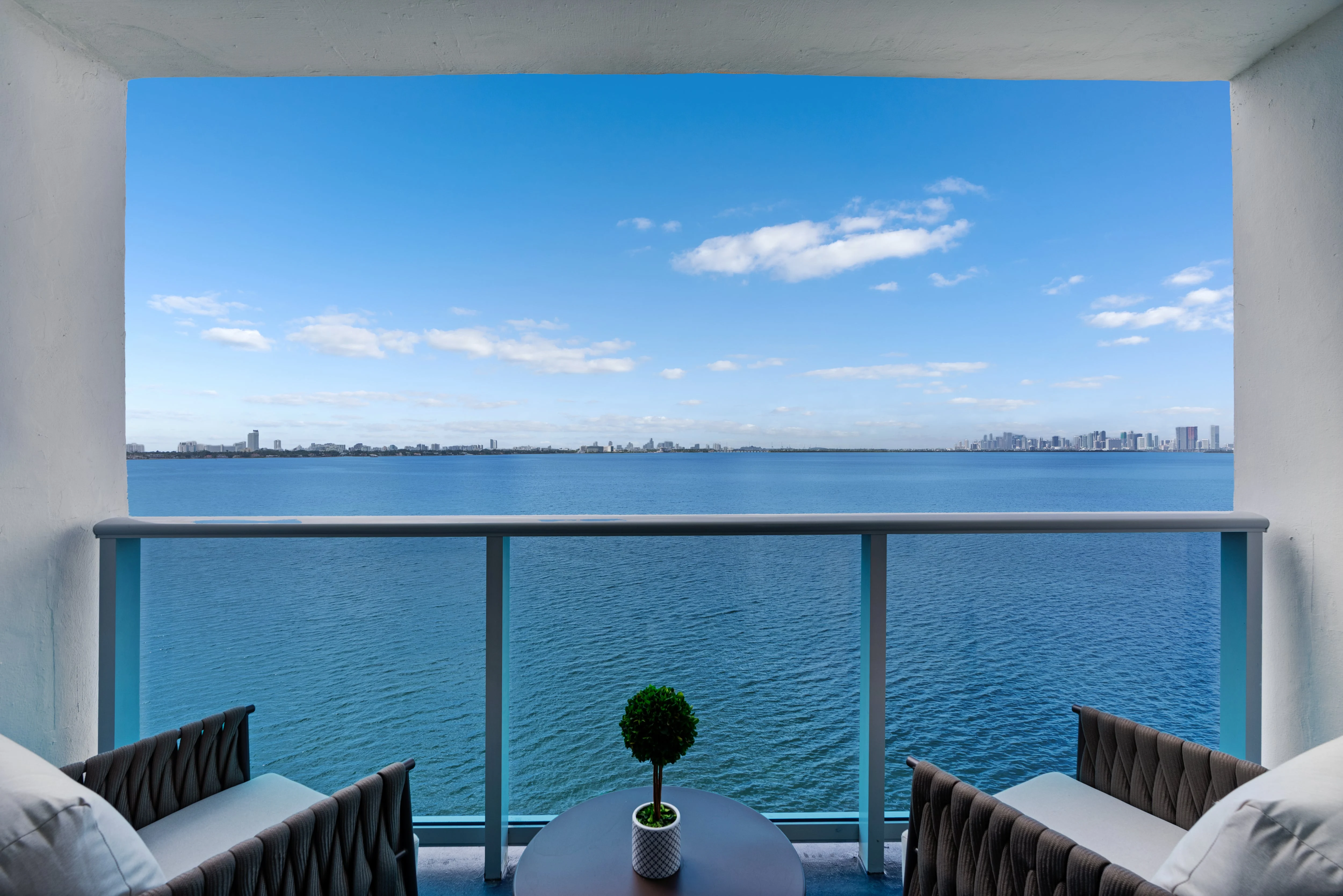 Serene Waterfront View from Balcony A view from a balcony overlooking calm water with a distant city skyline under a clear blue sky.