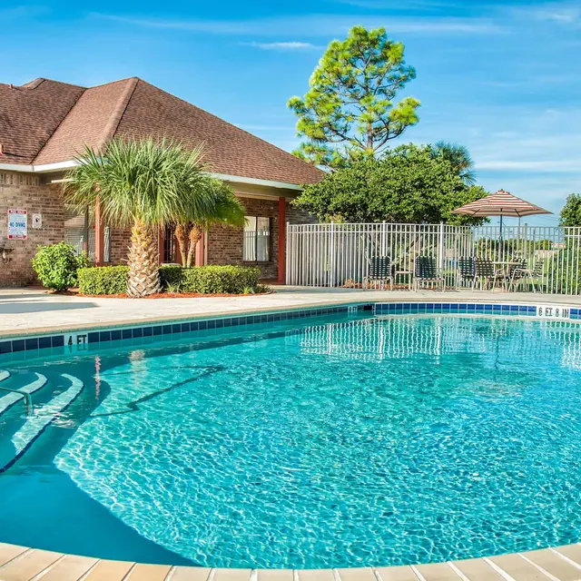 A swimming pool with a surrounded by a white fence, with a clear blue sky.