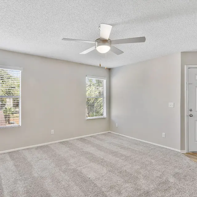 A spacious bedroom featuring two windows, a ceiling fan, and carpeted floors.