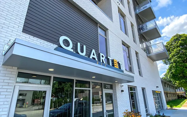 Exterior of a modern building named QUARTET with glass doors, balconies above, under a clear blue sky.