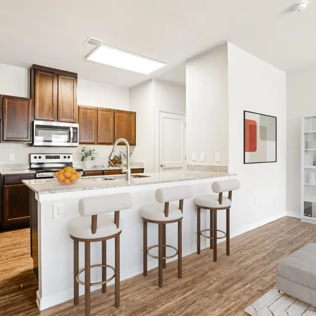 Contemporary Kitchen Design A modern kitchen featuring dark wood cabinets, stainless steel appliances, and a breakfast bar with four stools. The space is well-lit, with a dining area and a contemporary decor style.