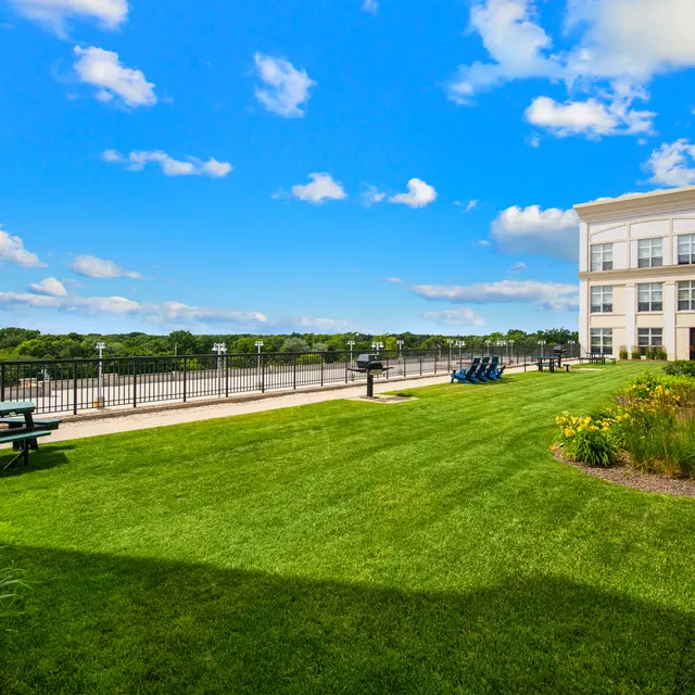 A lush green lawn next to a river with a modern building in the background and picnic tables.