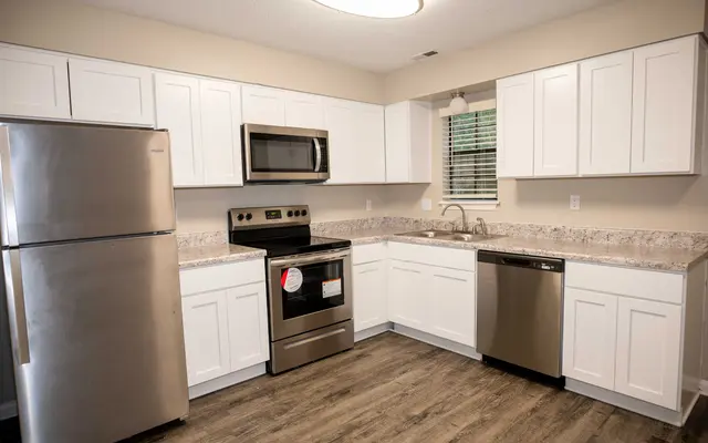 Summit at 501 Modern kitchen with stainless steel appliances, white cabinetry, gray countertops, and wood-style flooring. Bright and clean design.