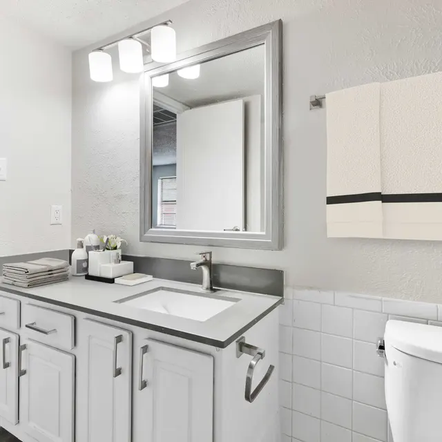 Apartment bathroom with sink with overhead lighting, toilet, and half tiled wall
