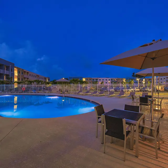Pine Groves Evening view of the fenced in pool with lights, lounge chairs and tables surrounding the pool at Pine Groves