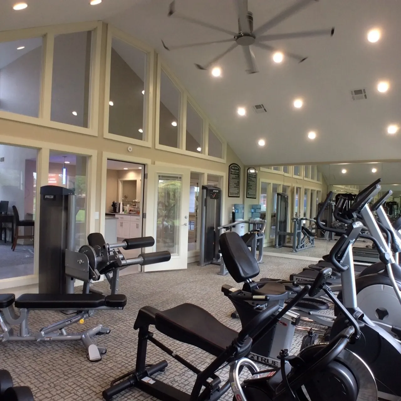 The Hunt A spacious gym with various exercise equipment including treadmills, stationary bikes, and weight machines, surrounded by mirrors and large windows.