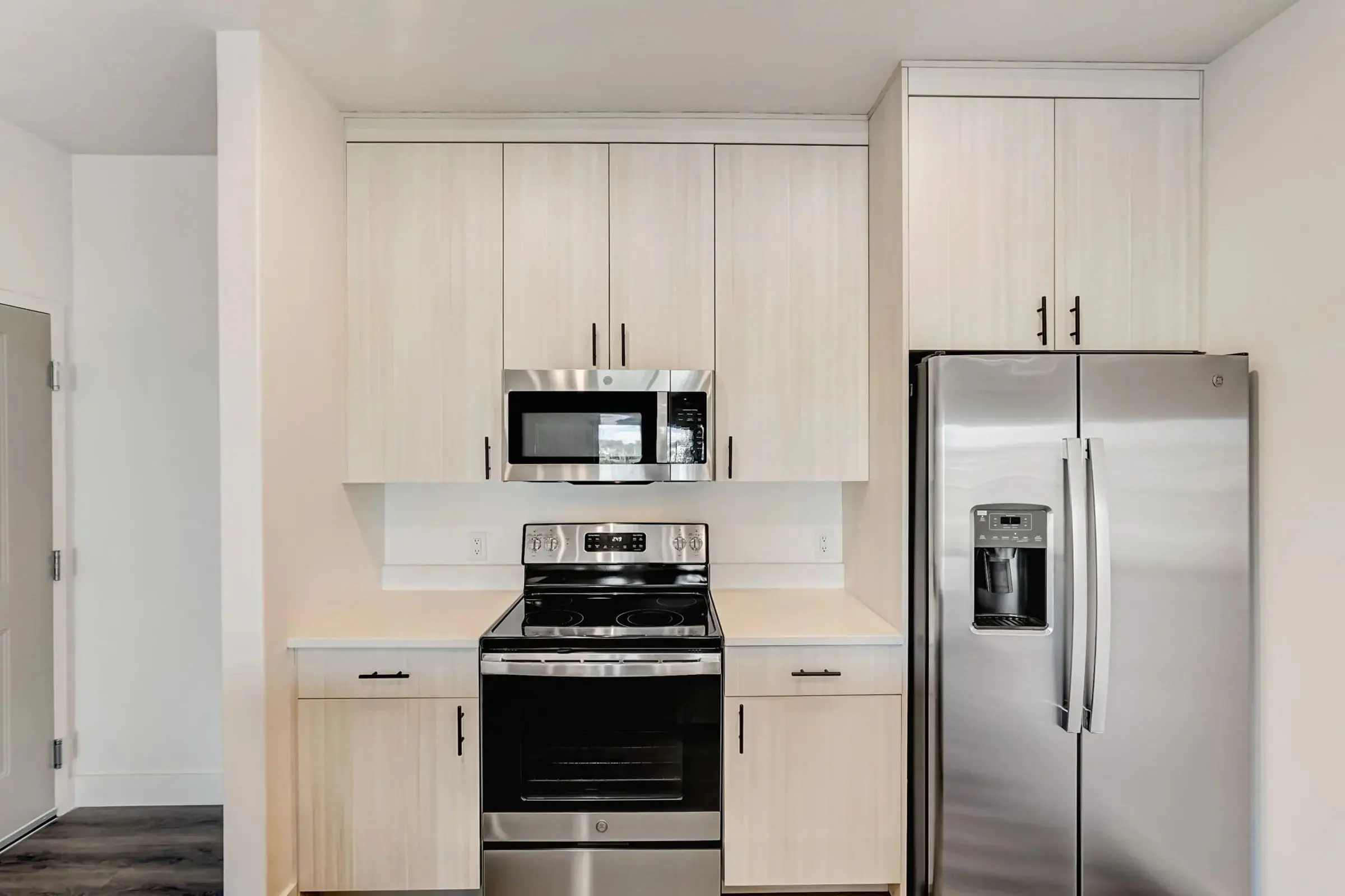 A modern kitchen featuring light-colored wooden cabinets, stainless steel appliances including an oven and a refrigerator, and a clean countertop.