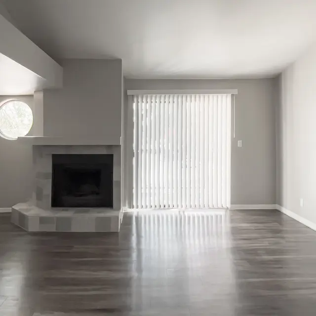 Modern living room with gray walls, hardwood floors, a circular window, and a fireplace, featuring vertical blinds.