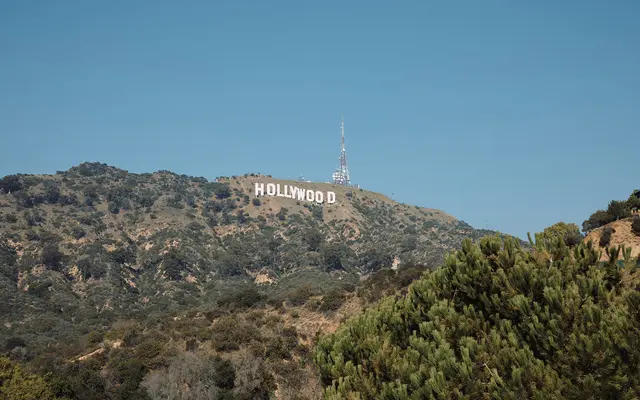 View of the Hollywood Sign on a hillside, surrounded by greenery and blue sky.