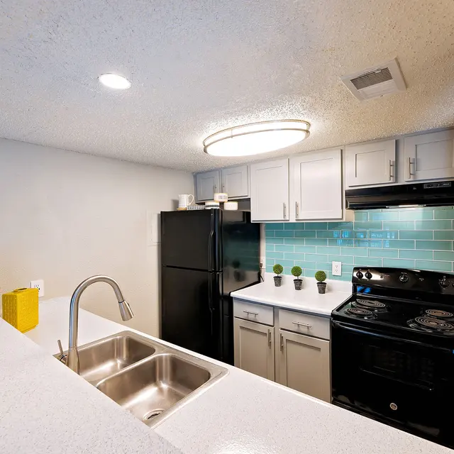 Artisan at South Lamar Kitchen with white cabinets, black appliances, and a double sink on a raised dining bar