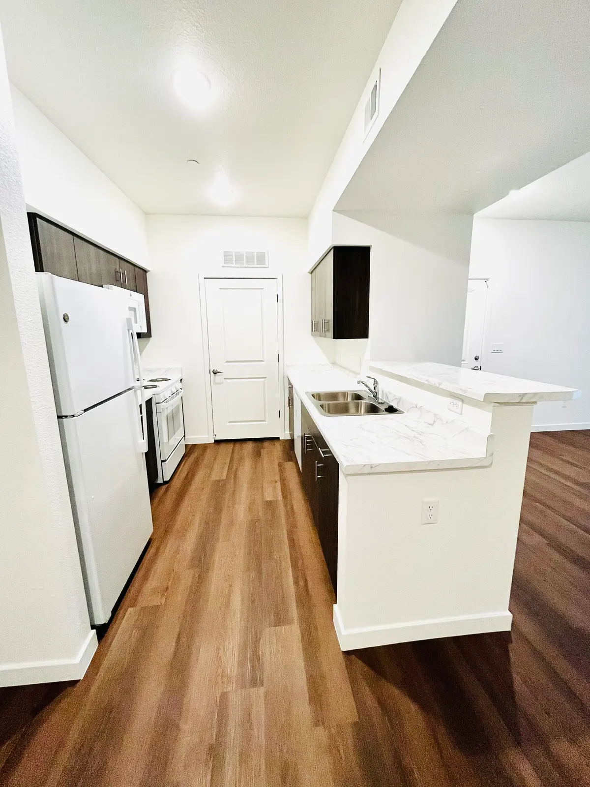 Kitchen with white appliances, dark cabinets and a sink counter.