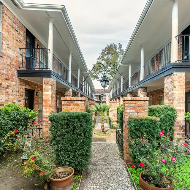 A view of a courtyard in an apartment complex featuring brick buildings, a pathway, and greenery.