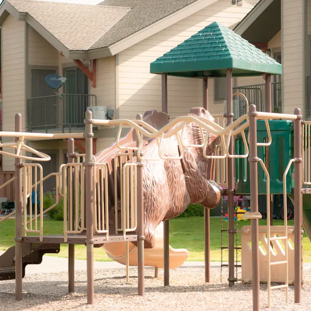 Playground with Bear-Shaped Play Structure A playground with climbing structures and slides, featuring a large bear-shaped play structure in the center. Surrounding the playground are several apartment buildings with balconies.