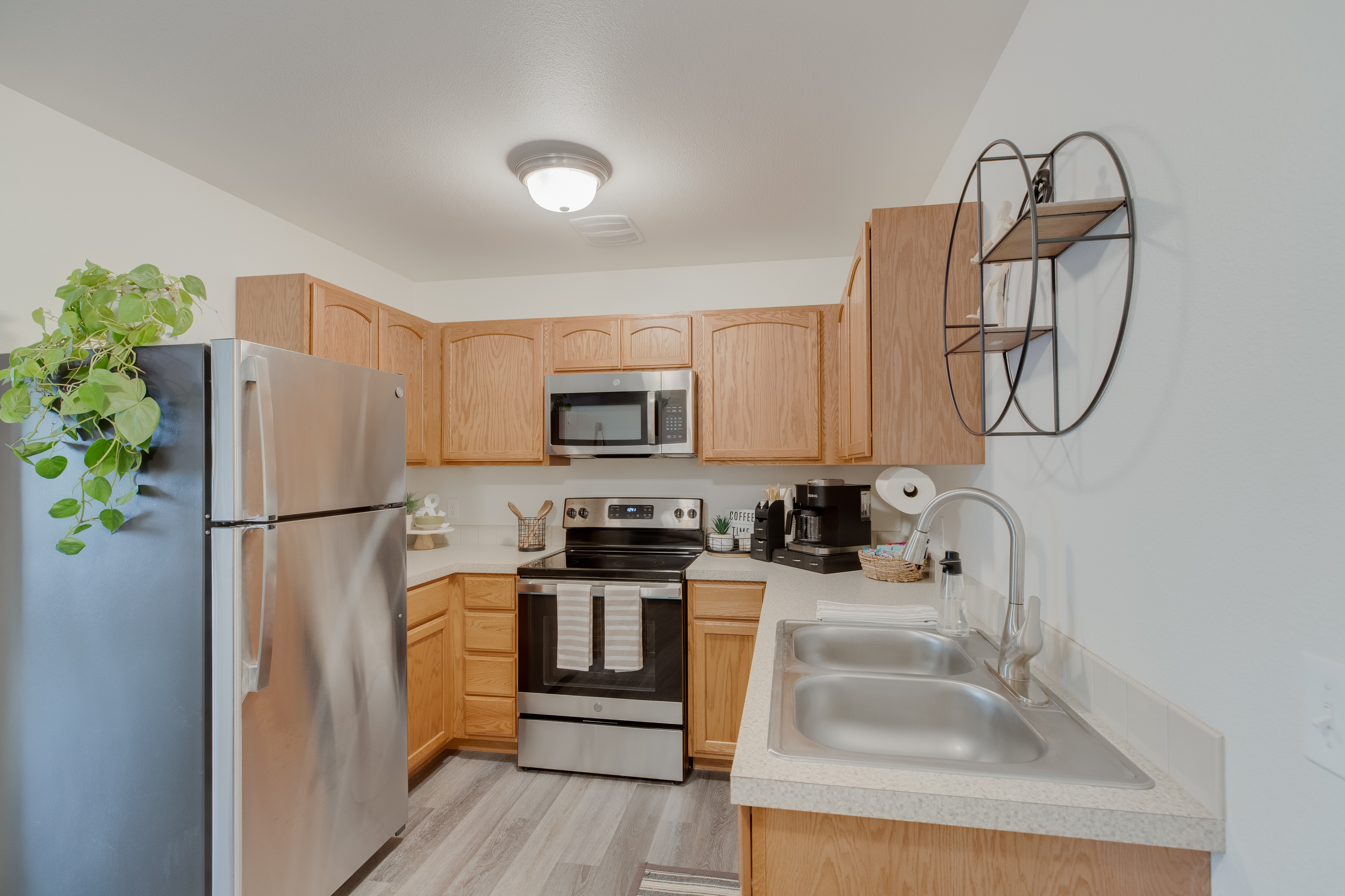 Modern apartment kitchen at The Landing at Clearwater in Moscow, Idaho, featuring stainless steel appliances, wood cabinetry, double-basin sink, and stylish decor. A spacious layout with ample counter space provides both functionality and modern convenience.