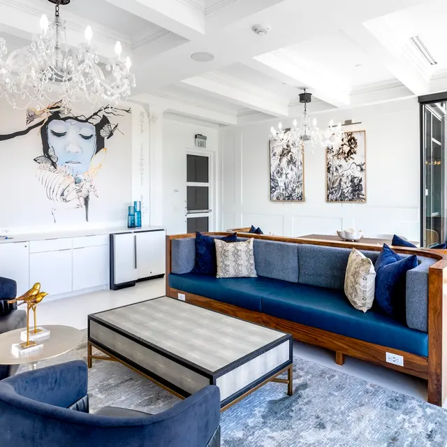 Luxurious living room featuring modern decor, blue couch, elegant chandeliers, and artistic wall art, creating a stylish ambiance.