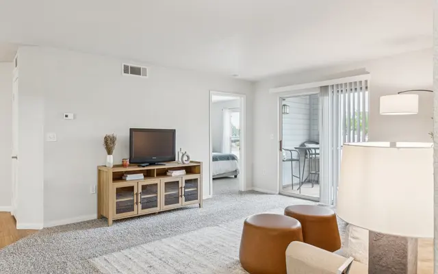 A modern living room featuring a TV stand, round ottomans, and a sliding glass door leading to a balcony.