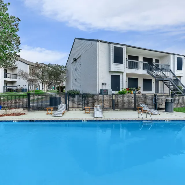 Fenced-in community pool with lounge chairs and small tables next to chairs. 