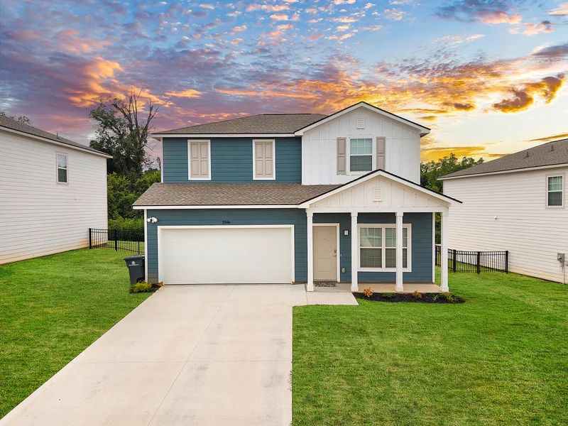 Modern Two-Story House at Sunset A modern two-story house with blue and white exterior, a driveway, and a grassy yard at sunset.