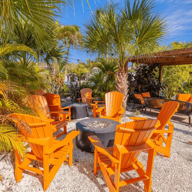 Tropical Outdoor Seating Area A cozy outdoor seating area surrounded by palm trees with orange Adirondack chairs arranged around a circular fire pit.