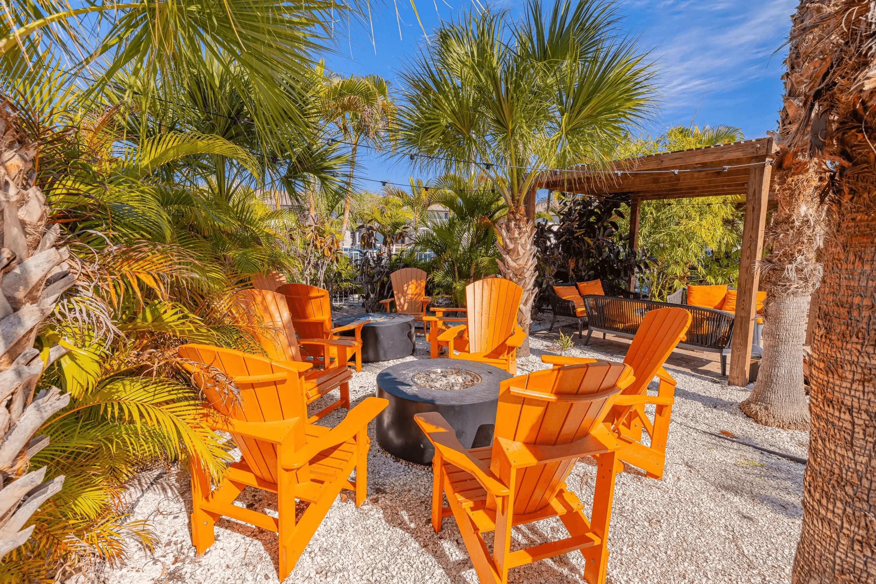 Tropical Outdoor Seating Area A cozy outdoor seating area surrounded by palm trees with orange Adirondack chairs arranged around a circular fire pit.