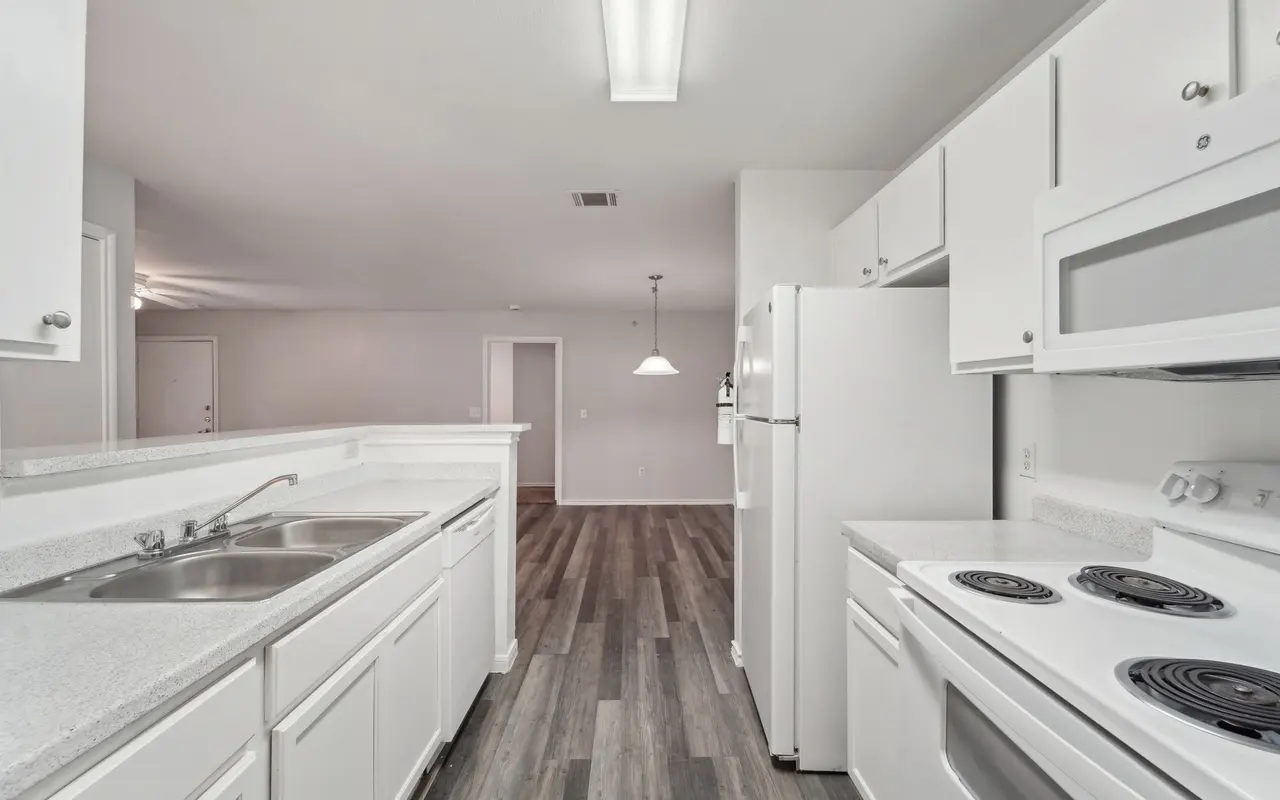 A modern kitchen featuring white cabinets, a double sink, and an electric stove, with gray laminate flooring and a spacious layout.