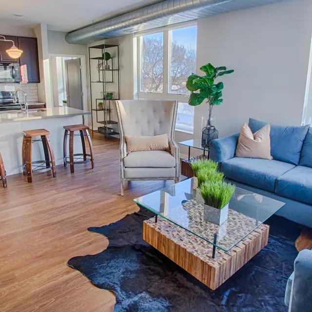 Open-concept apartment at Woodrow Apartments in Fargo featuring a modern kitchen with bar seating, a stylish living room with large windows, and contemporary furniture.