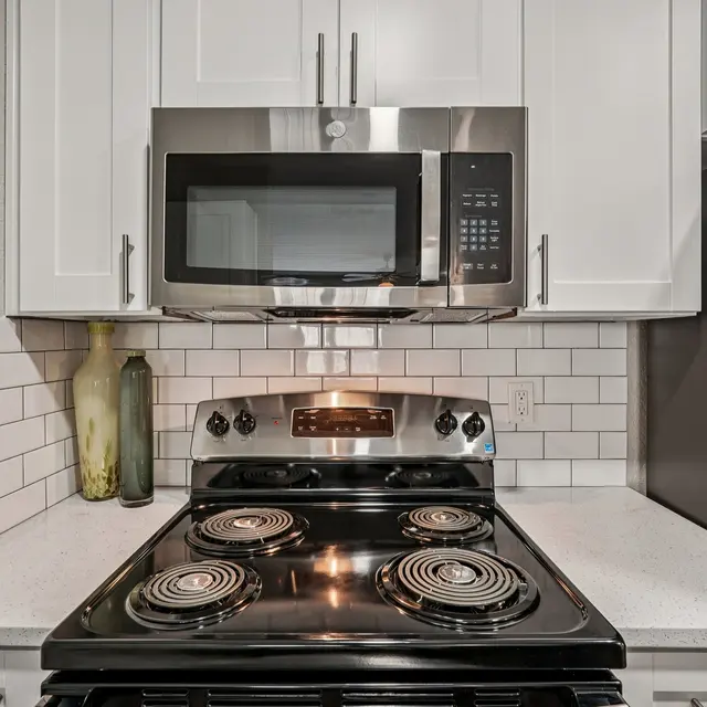 A modern kitchen featuring a stainless steel stove and microwave against a white tiled backsplash.