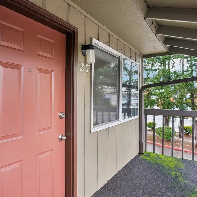 Exterior view of an apartment entrance with a pink door and a small patio area.