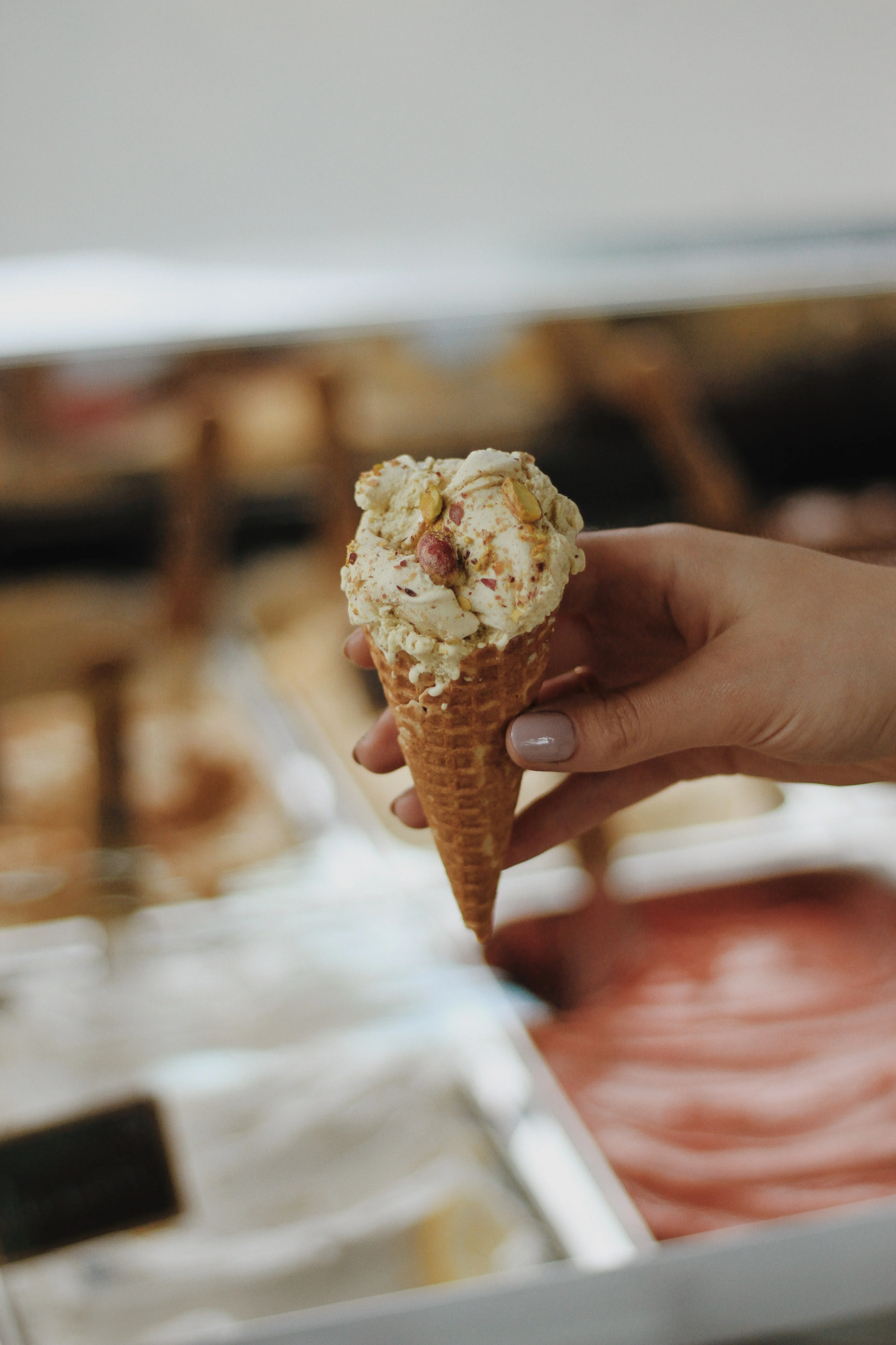 Ice Cream Delight A hand holding a cone of ice cream with colorful sprinkles, standing in front of a display of gelato flavors.