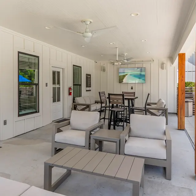 Outdoor Lounge Area An outdoor lounge area featuring comfortable seating, a table, and a light-colored building facade with wooden pillars.